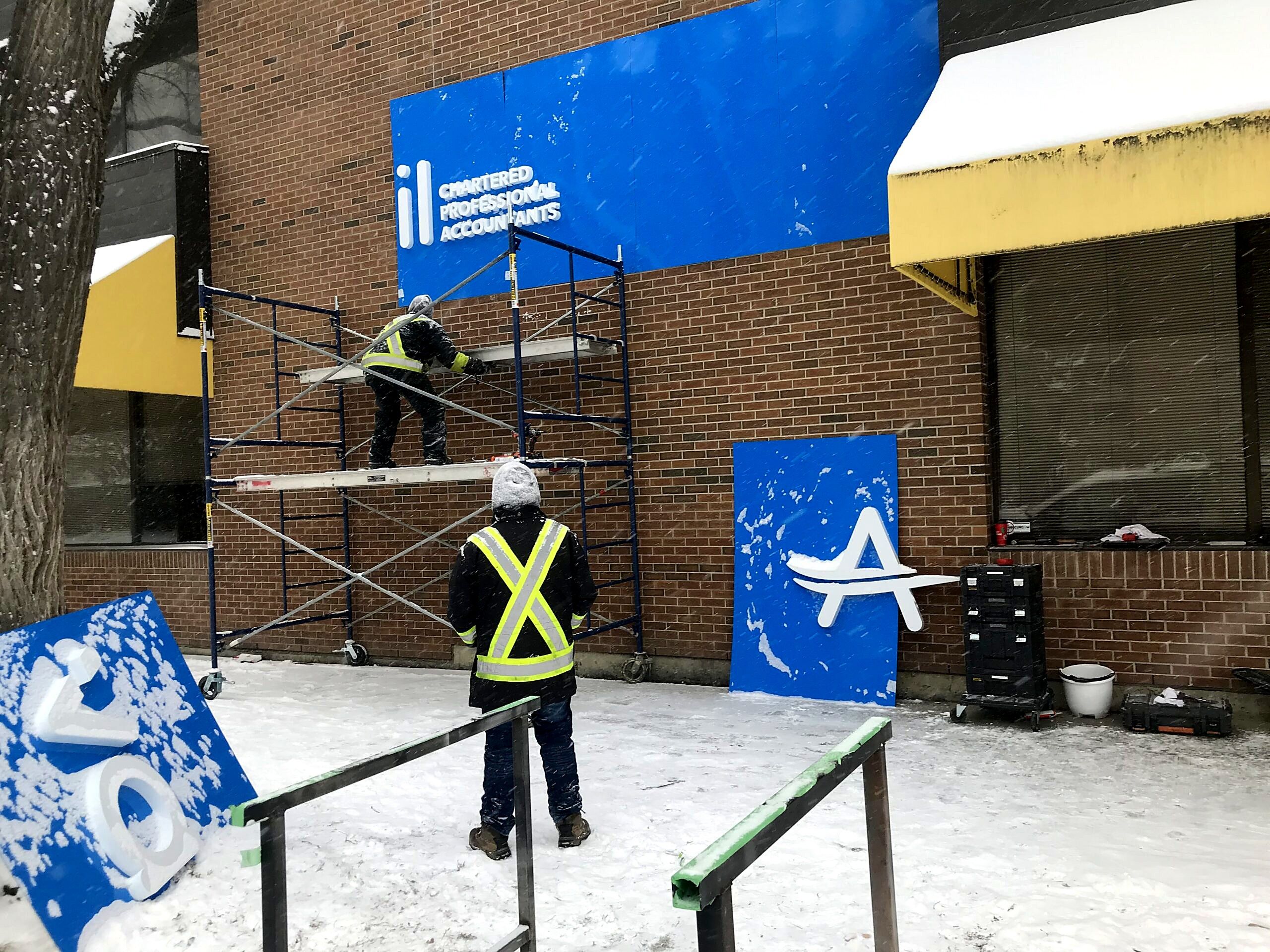 Two installers on scaffolding mounting the Avail CPA fascia panels on a brick building in winter